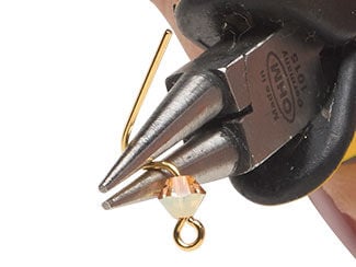 Pliers bend a wire into a curve to form a loop at the end of an eye pin with a bicone bead on it.